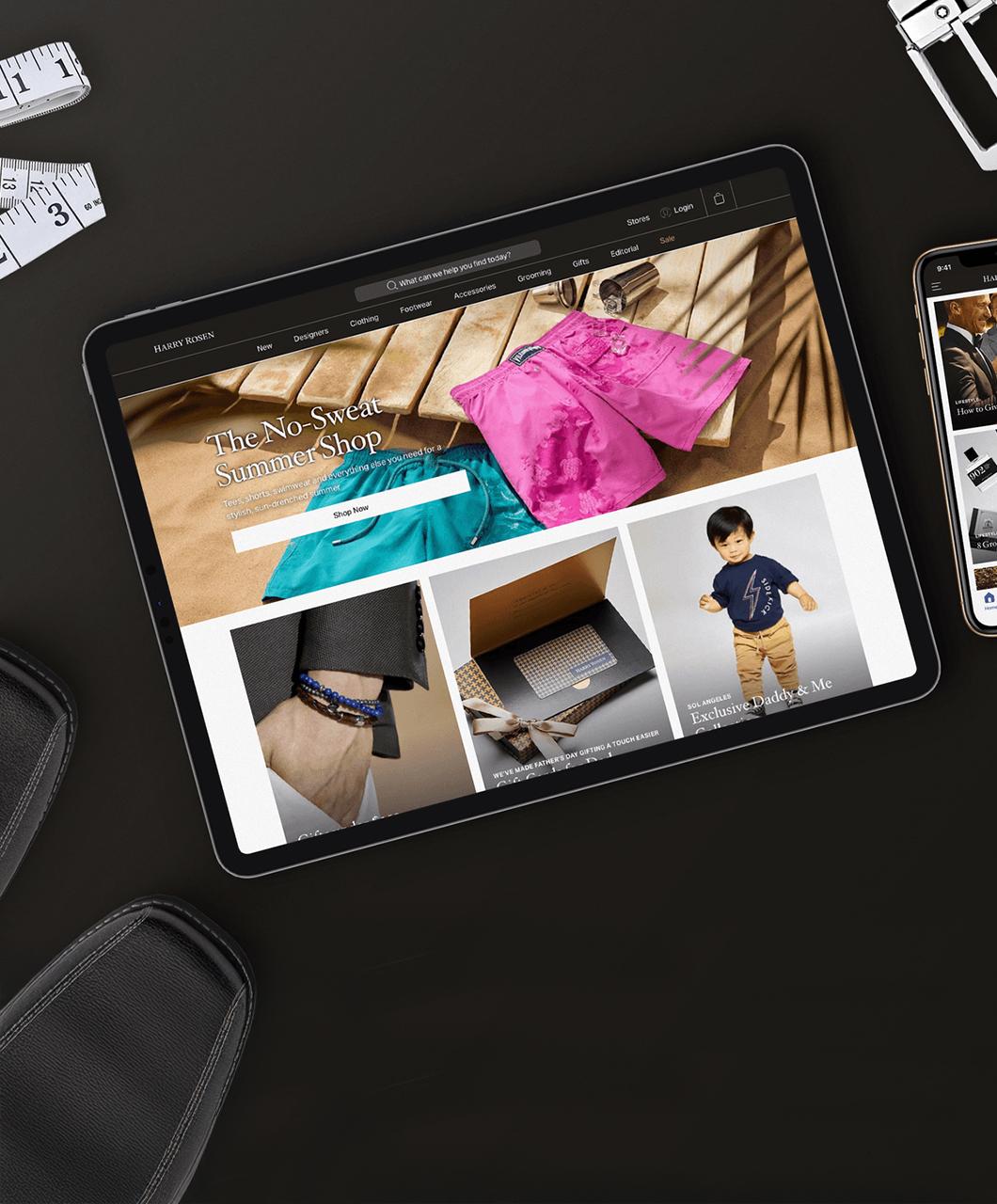 Tablet displaying an online fashion store featuring summer clothing and accessories, placed on a black desk with measuring tape and other items nearby.